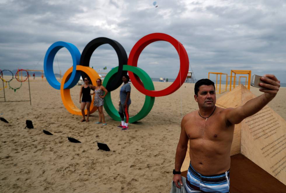 Homem faz um selfie em frente ao símbolo das Olimpíadas em Copacabana.