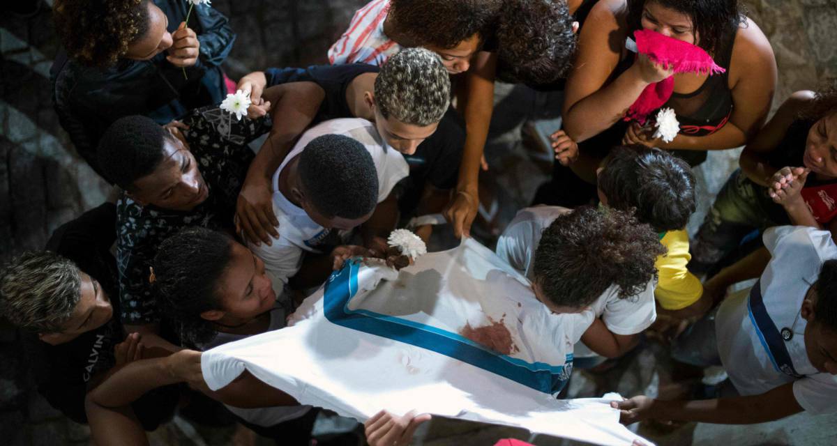 Amigos e familiares de Marcos Vinícios choram sobre sua camiseta da escola manchada de sangue, nesta quinta-feira.