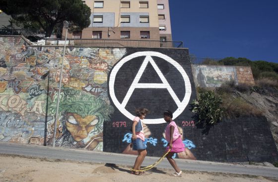 Dos niñas juegan ante un símbolo anarquista, la A de Can Franquesa, en un muro de Barcelona.