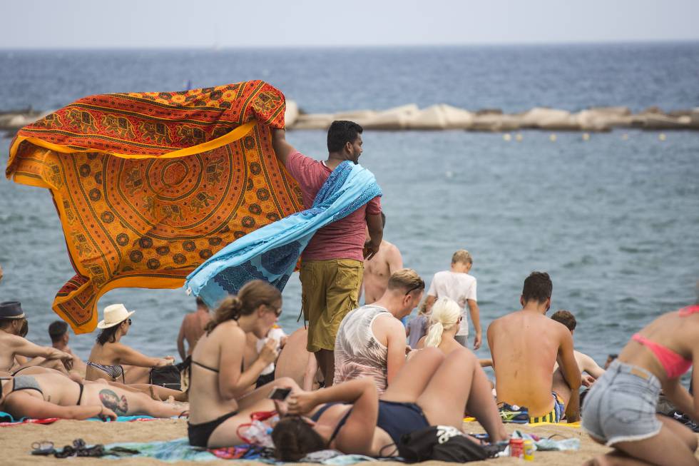 Un home ven pareos a la platja de la Barceloneta.