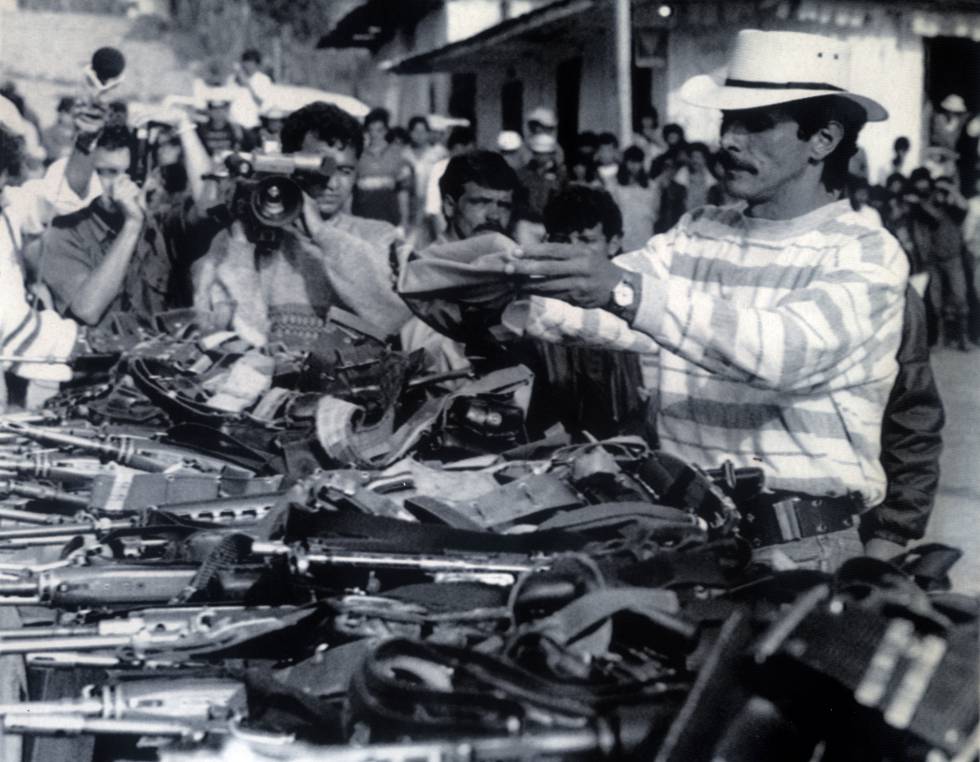 Carlos Pizarro, líder del M-19, envuelve su pistola en una bandera colombiana en el acto de entrega de armas del grupo guerrillero, en marzo de 1990.