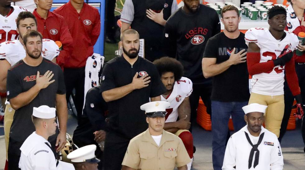Colin Kaepernick espera sentado mientras suena el himno estadounidense antes de un partido de pretemporada de los San Francisco 49ers.
