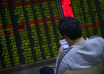 Un inversor mira su telef&oacute;no m&oacute;vil frente a un panel de cotizaciones en Pekin.  AFP PHOTO  WANG Zhao