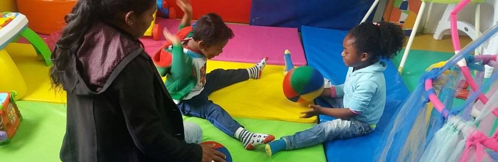 Una monitora juega con dos niños en el jardín de Laudes Infantis de Bogotá.