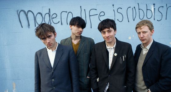 Os quatro membros de Blur, com Damon Albarn à esquerda, retratados em 1994 em frente a uma frase com o nome de seu segundo disco.