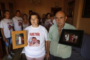 Father Toño’s parents hold up photos of their son, with the rest of the family behind them.