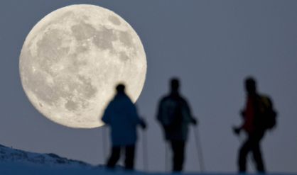 Tres esquiadores contemplan la luna llena en el Weissfluhjoch (Suiza).