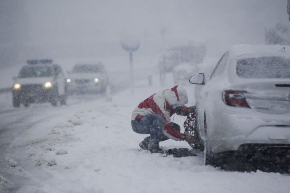 A man fits snow chains on his car in Lugo province.