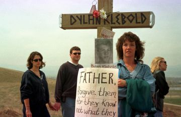 Pessoas visitando o ponto no qual foi feita uma homenagem às vítimas do massacre de Columbine, em Littleton, Colorado. Na imagem, una cruz com a foto e o nome de Dylan Klebold e um cartaz no qual se lê: “Pai, perdoai-os porque eles não sabem o que fazem