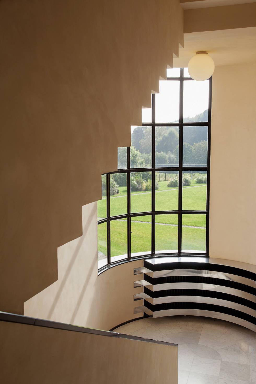 La escalera principal se ilumina gracias a un gran ventanal con vistas al jardín. Las líneas en aluminio del cubre-rradiador subrayan su diseño curvo.rn