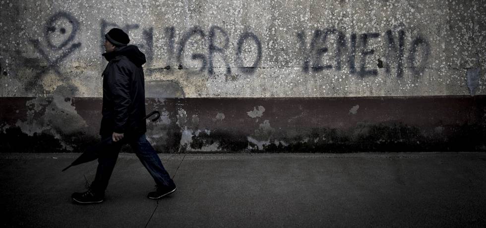 Un vecino cruza ante una pintada de advertencia sobre el lindano en las viviendas sociales de Torneiros, barrio de O Porriño.