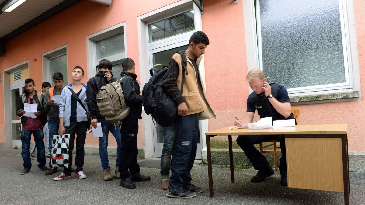 Un policía alemán registra a refugiados.
