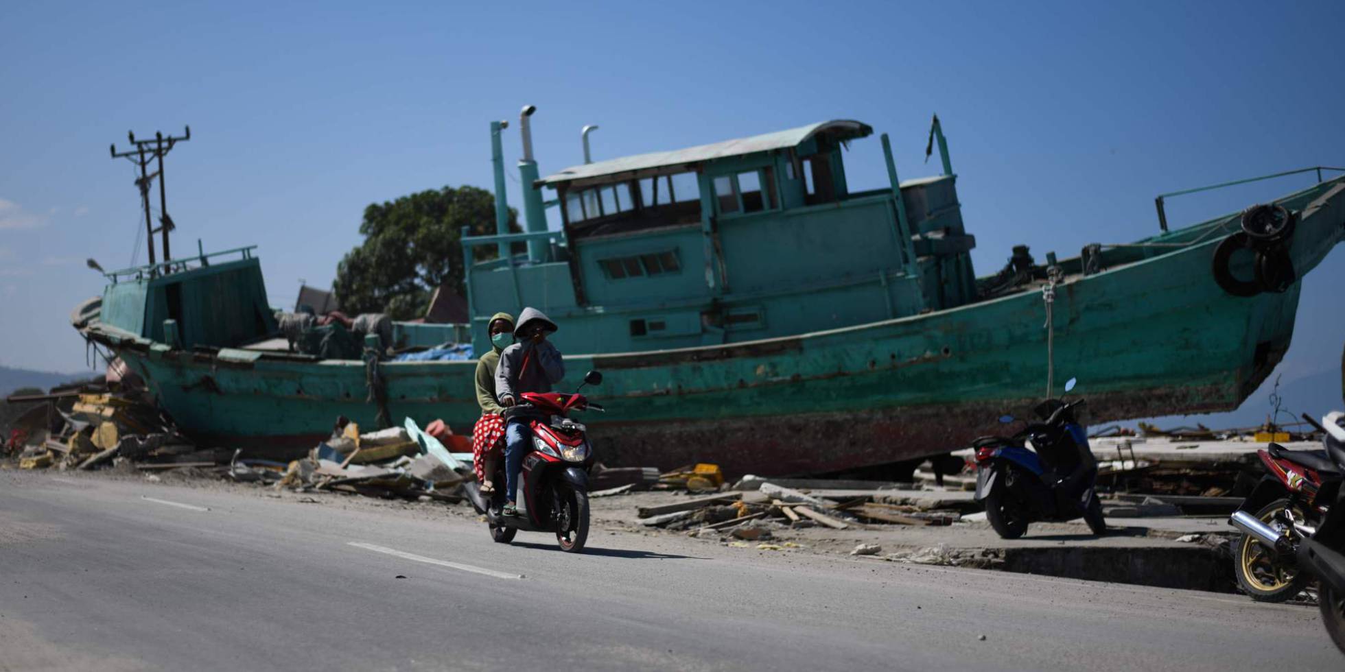 Supervivientes del terremoto en Indonesia pasan frente a un barco desplazado en mitad de una calle, en Palu.