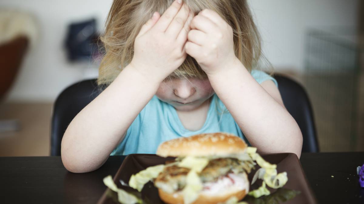Una niña no quiere comer una hamburguesa.