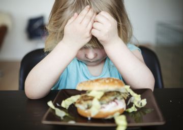 Una niña no quiere comer una hamburguesa.