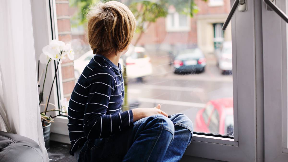 Un niño mira por la ventana de su cuarto.