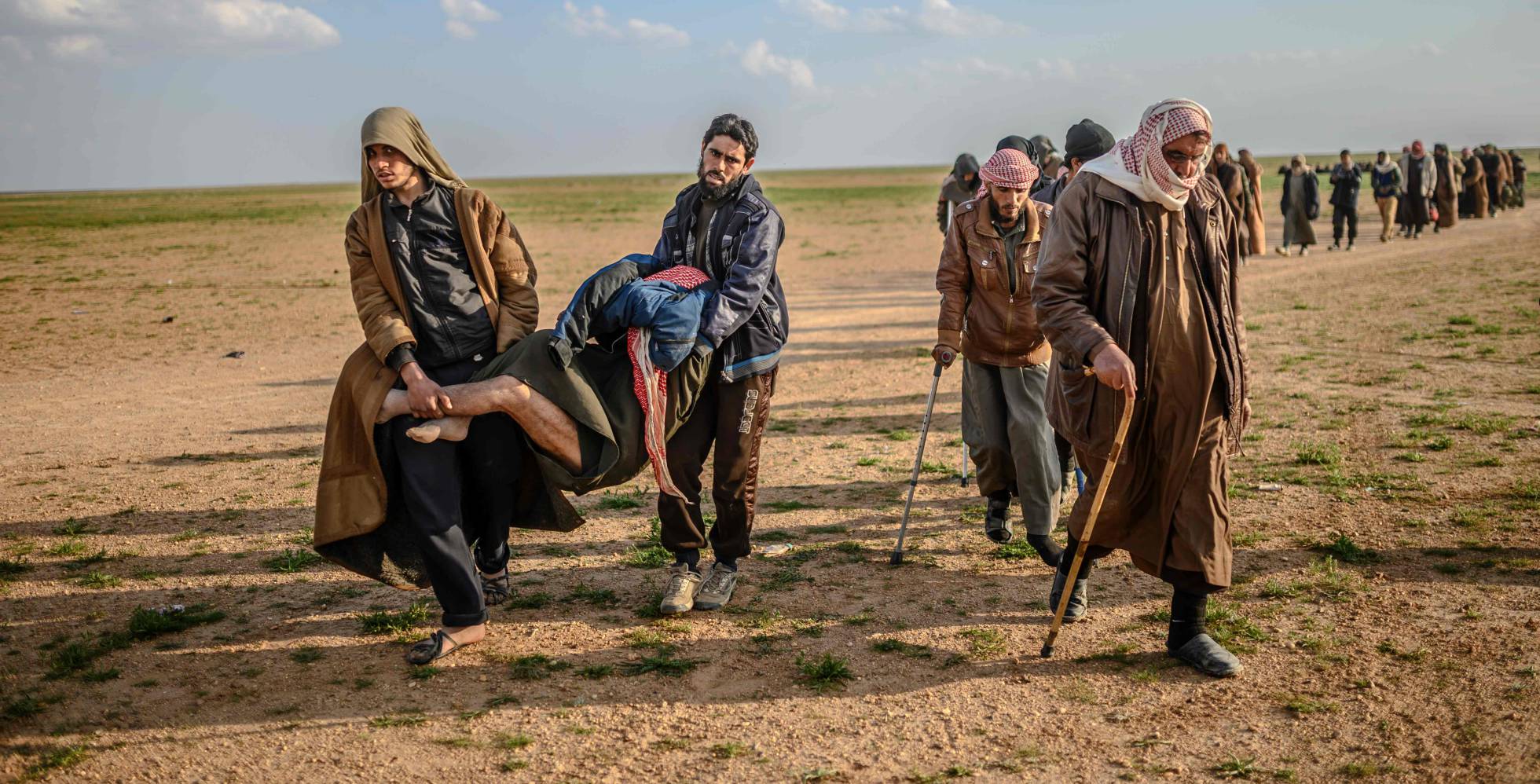 Varios hombres, sospechosos de pertenecer al Estado Islámico, sujetan un herido, mientras avanzan hacia las Fuerzas Democráticas Sirias, lideradas por los kurdos, tras abandonar Baghouz, en la provincia de Deir Ezzor, al norte de Siria.
