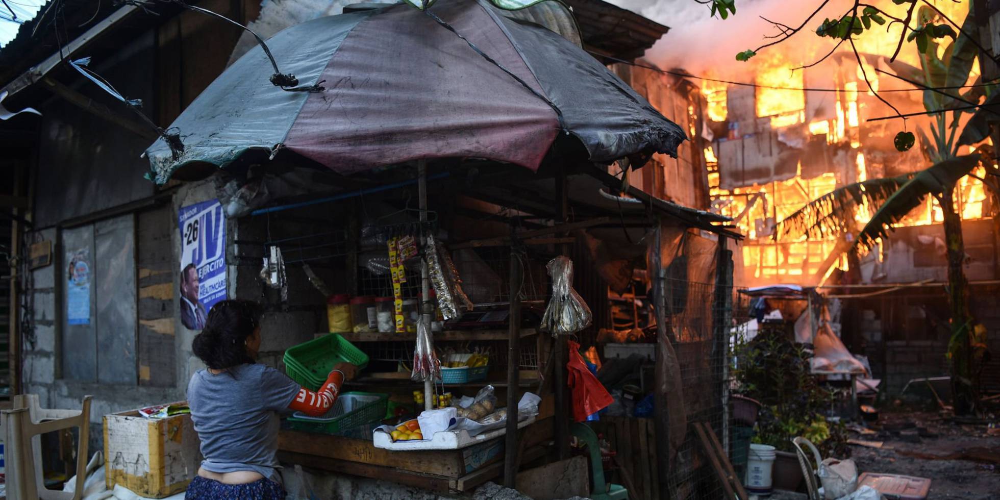 Una vendedora recoge sus bienes de un puesto próximo a una casa en llamas tras un incendio en el suburbio de Quezon (Manila).