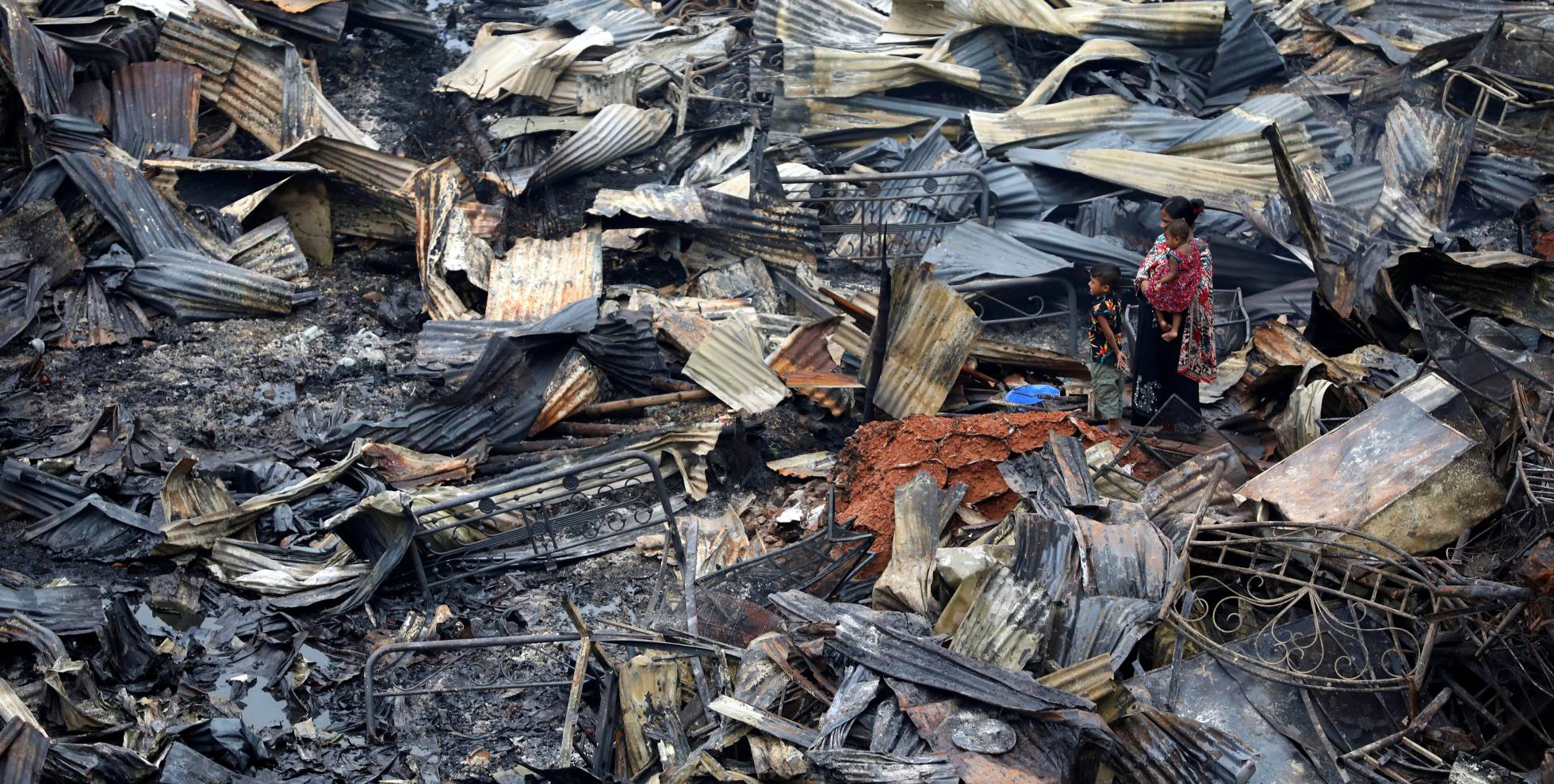 Una mujer con sus hijos regresan a sus refugios luego de que estos fueran devastados por un incendio en Daca (Bangladés), el 17 de agosto de 2019.