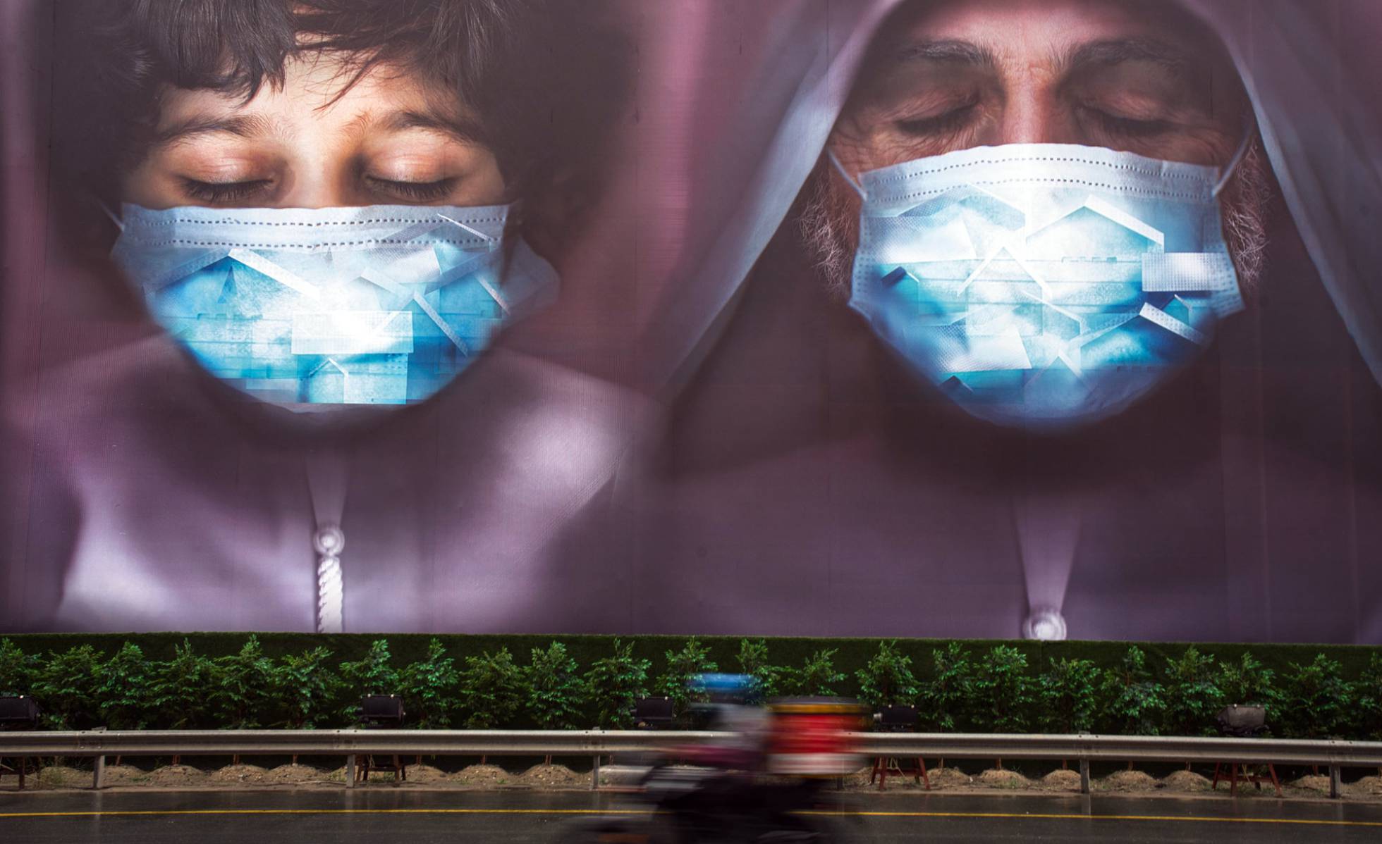 Un repartidor pasa junto a una valla publicitaria instando a las personas a utilizar mascarillas en Dubái (Emiratos Árabes).