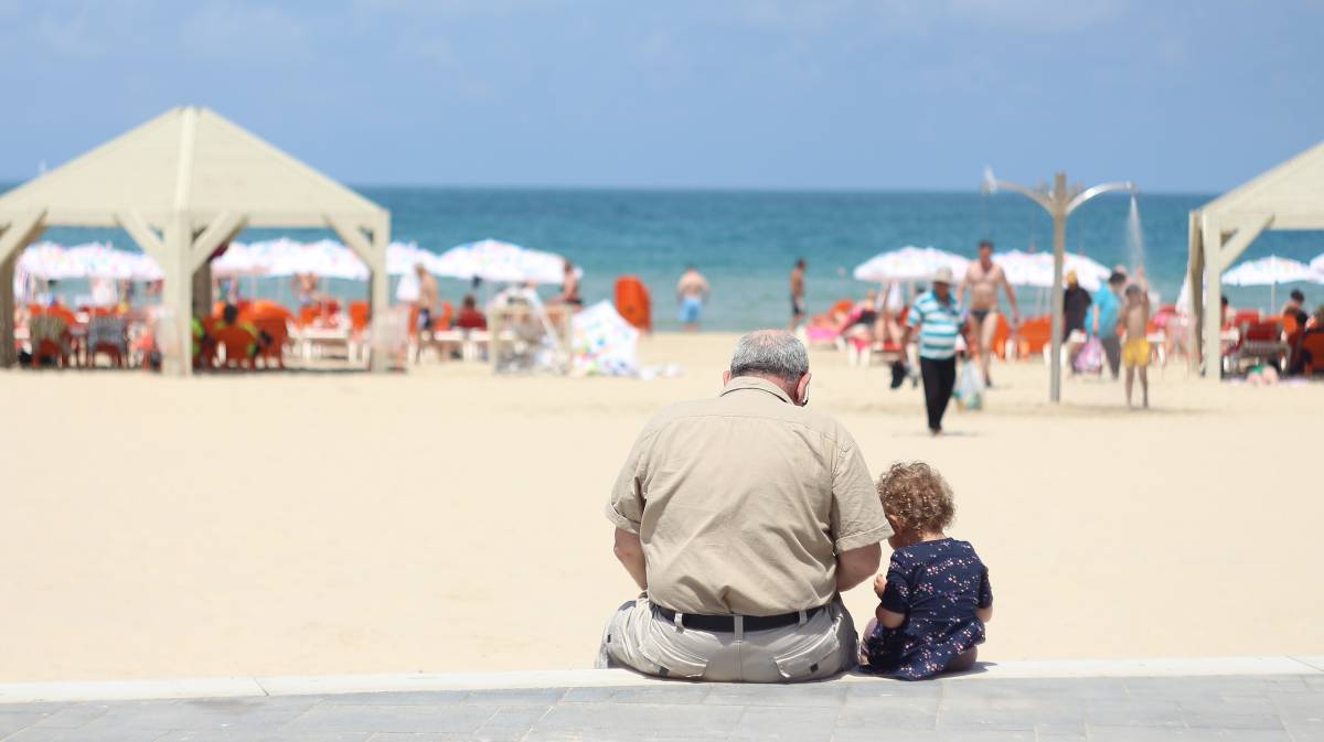 Un abuelo se sienta con su nieta en el poyete de un paseo marítimo.