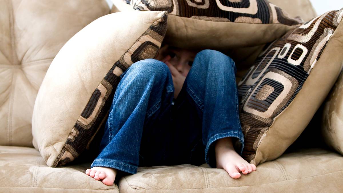 Un niño se esconde entre los cojines del sofá.