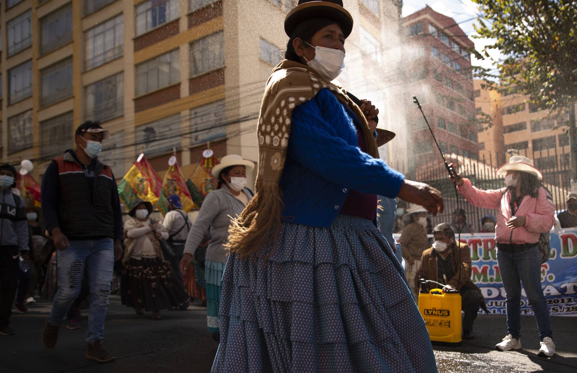 Una mujer rocía desinfectante a manifestantes en medio de la pandemia COVID-19, durante una marcha pidiendo acceso gratuito a internet y computadoras al gobierno, para que sus hijos puedan tomar clases en línea, en La Paz, Bolivia.