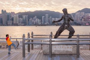 Un niño junto a la estatua de Bruce Lee ubicada en la Avenida de las Estrellas de Tsim Sha Tsui, frente al 'skyline' de Hong Kong.