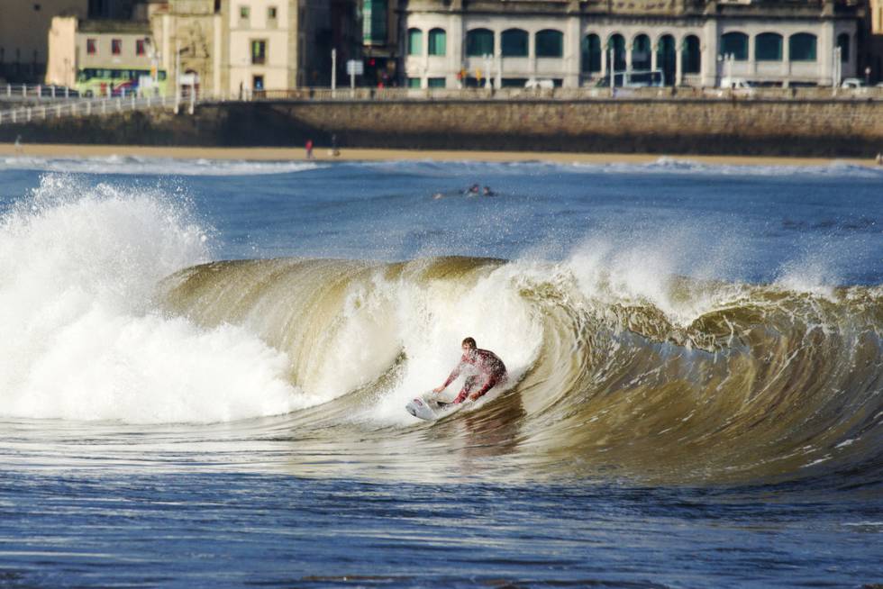 Un surfista sobre una ola en la playa gijonesa de San Lorenzo