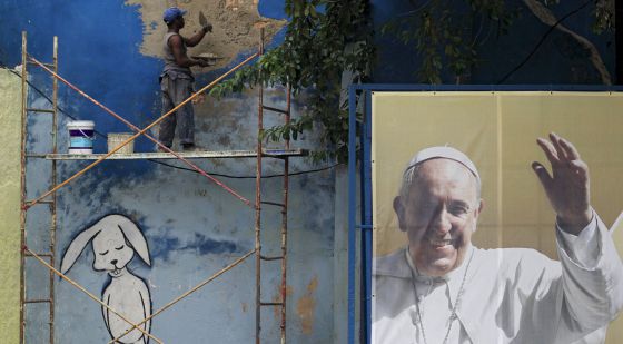 Un obrero repara un muro junto a un cartel del Papa. / REUTERS