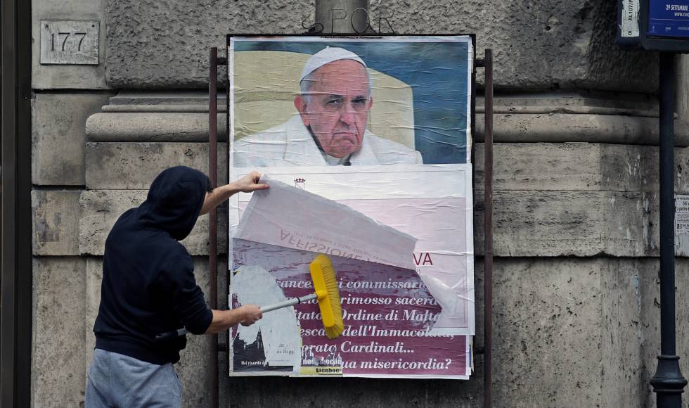 Um operário cobre um cartaz contra o Papa em uma rua de Roma.