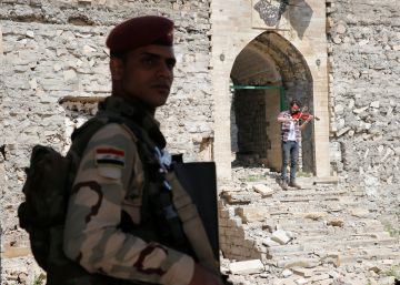 Un militar hace guardia en unas ruinas en Mosul. De fondo, un violinista que vivió bajo el régimen del ISIS toca una pieza.