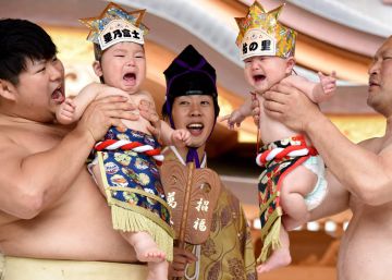 Una pareja de sumos sostiene en alto a dos bebés en un ritual celebrado en Japón.