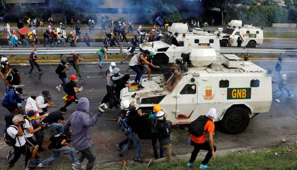 Varios manifestantes se enfrentan a un coche blindado de la policía durante una protesta en Caracas, el 1 de mayo de 2017.