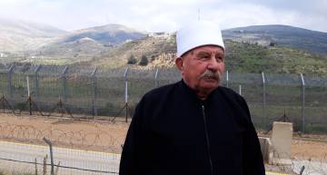 The Druze spiritual leader Jad al Karim Nbader, before the separation barrier with Syria in Majdal Shams. In the background, the Syrian military base on the shouting hill