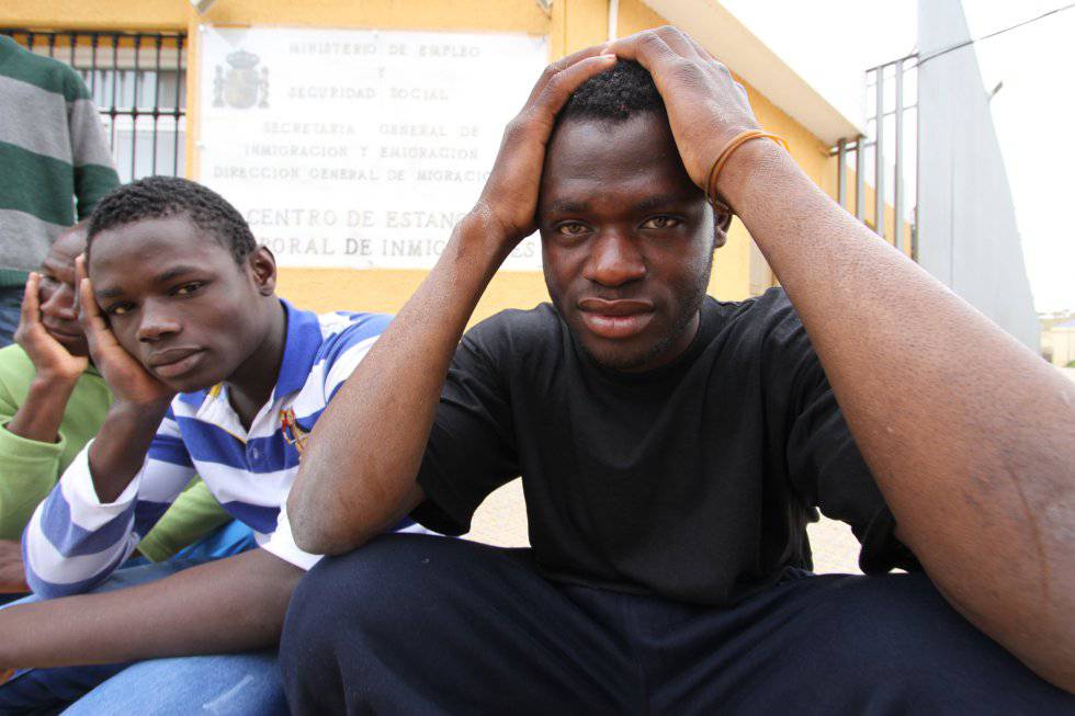 Un grupo de inmigrantes subsaharianos sentados frente a la puerta del CETI de Melilla.
