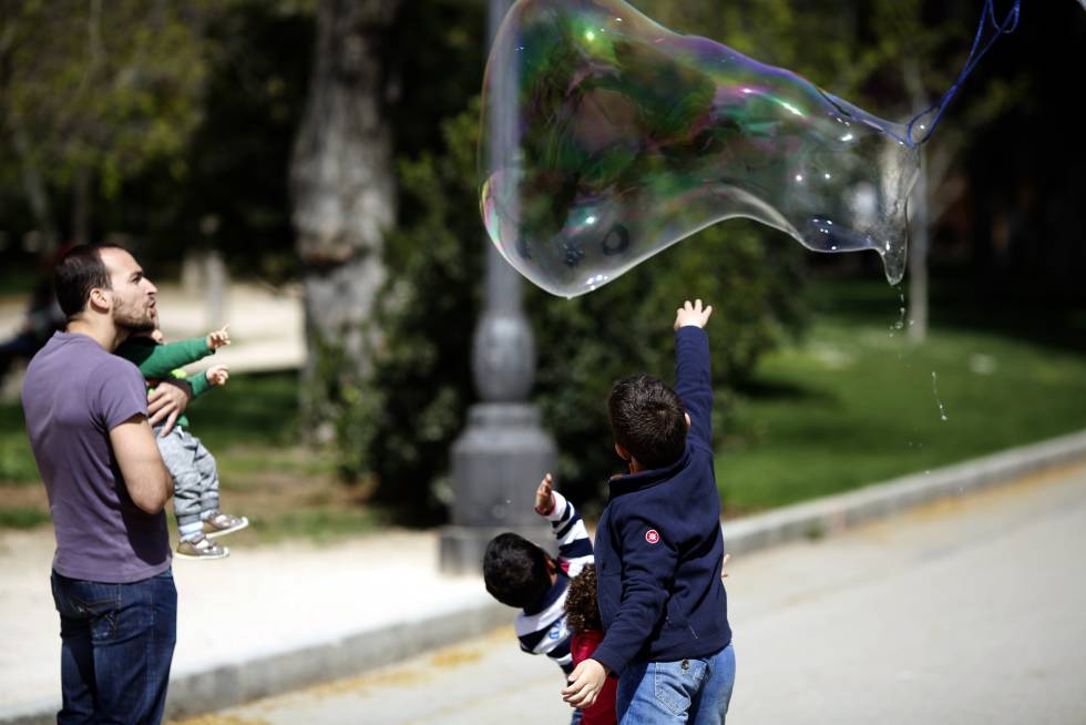 Un hombre y cuatro niños juegan con una pompa de jabón en el parque del Retiro de Madrid.