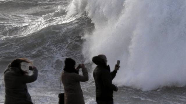 Varios turistas graban las olas ayer en la costa de Muxía.