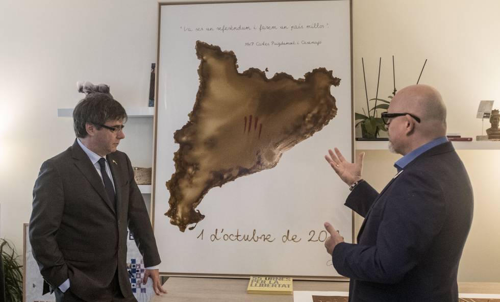 Puigdemont escolta l'explicació sobre una de les obres que li han regalat, a Waterloo (Bèlgica).