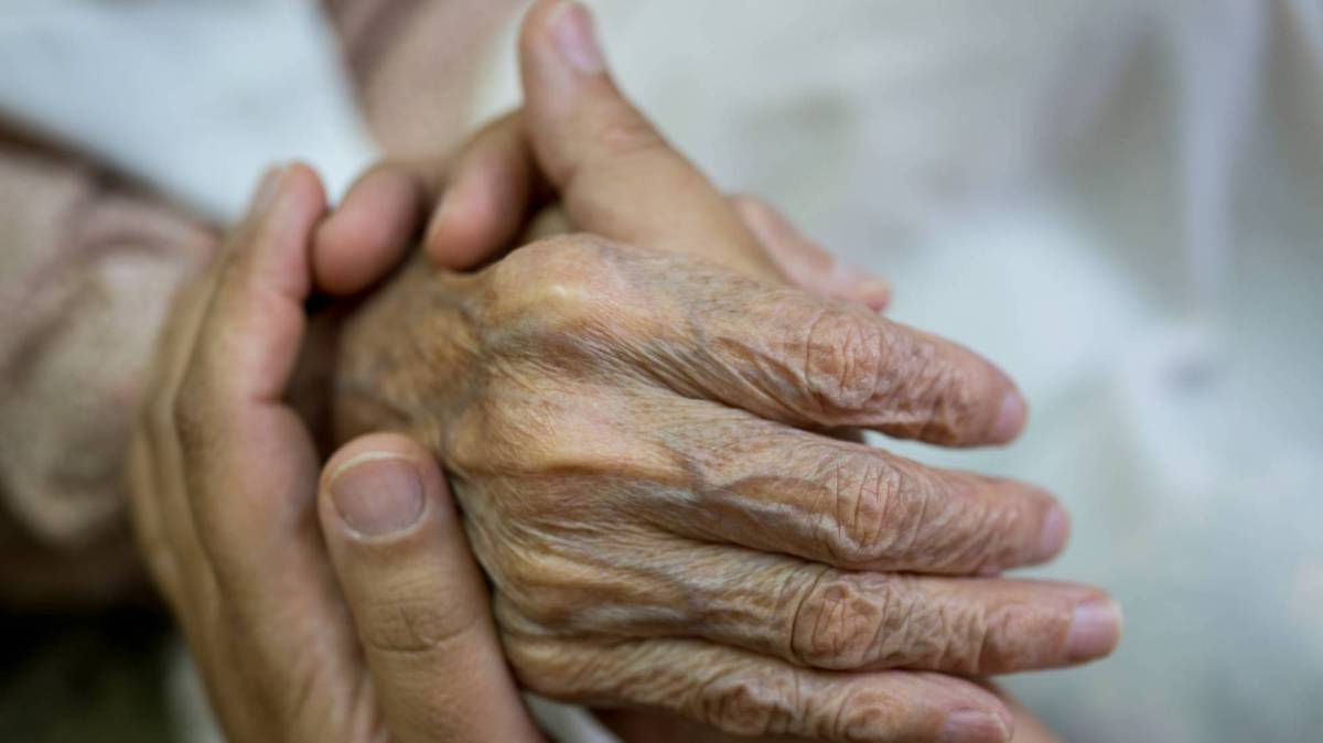 Una persona toma la mano de un anciano.