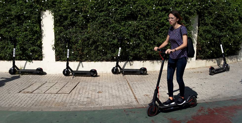 Una usuaria de patineta circula junto a cuatro unidades de uso compartido aparcadas en una acera de Sevilla