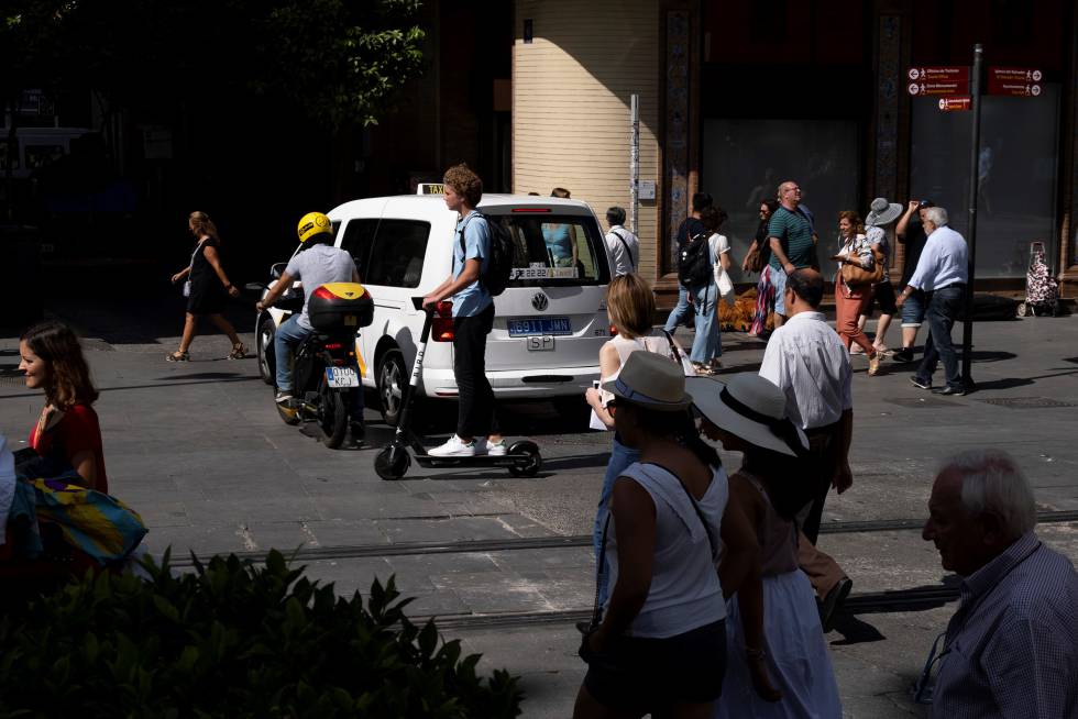 Un conductor de patinete comparte espacio con motos, vehículos y peatones.