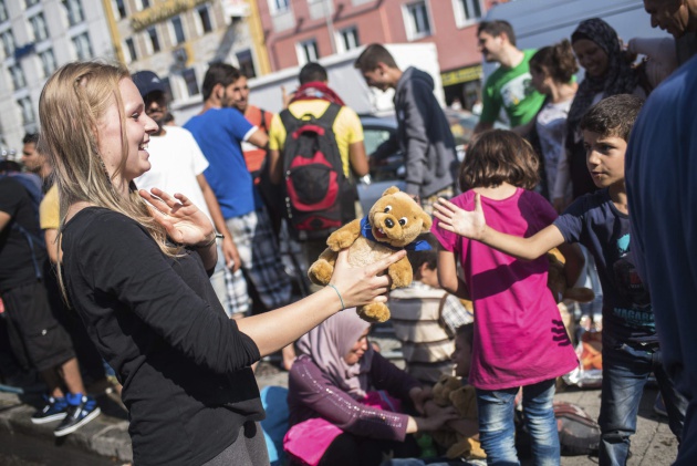 Una trabajadora de la iniciativa 'Ayuda a los Refugiados en Múnich' entrega un oso de peluche a un niño que espera con su familia un medio de transporte para acudir a uno de los centros de refugiados en la estación de Múnich (Alemania) 