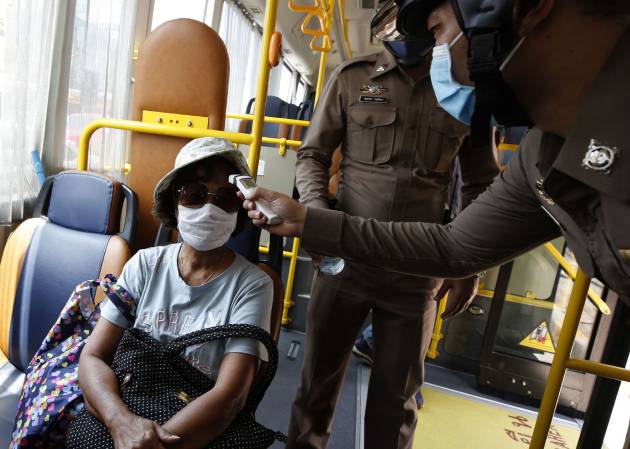 Un policía toma la temperatura de los viajeros de un autobús en la provincia de Bangkok Un policía toma la temperatura de los viajeros de un autobús en la provincia de Bangkok