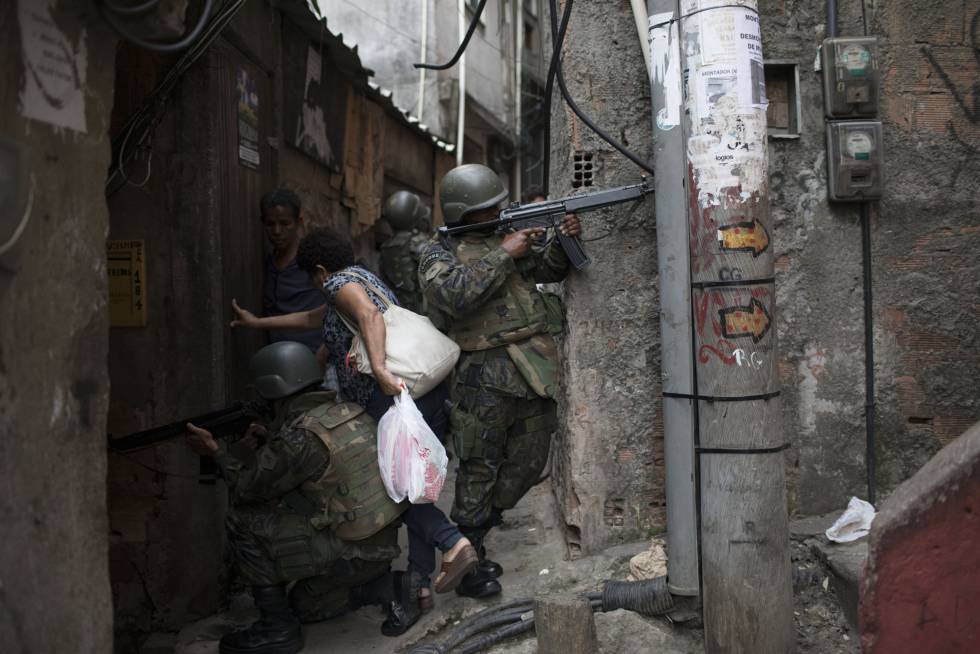 Mulher desliza entre soldados para ultrapassar uma barreira armada em um beco da Rocinha.