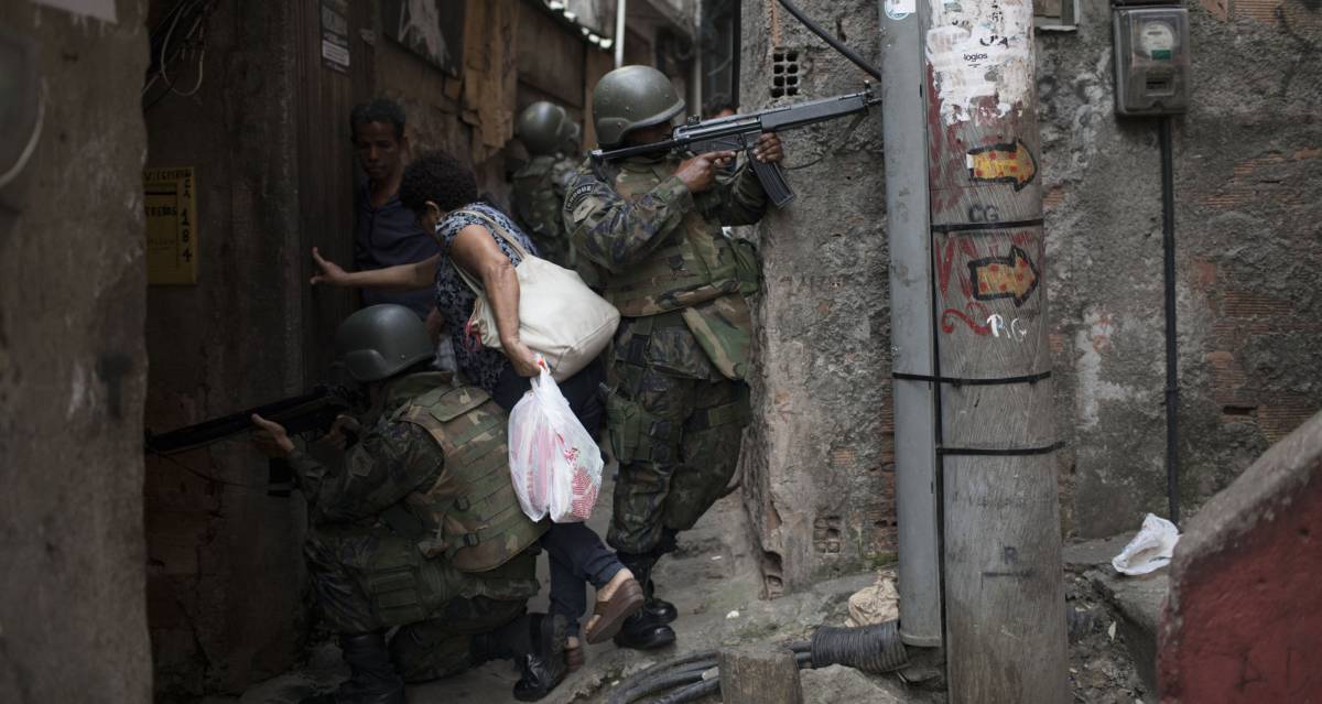 Mulher desliza entre soldados para ultrapassar uma barreira armada em um beco da Rocinha.