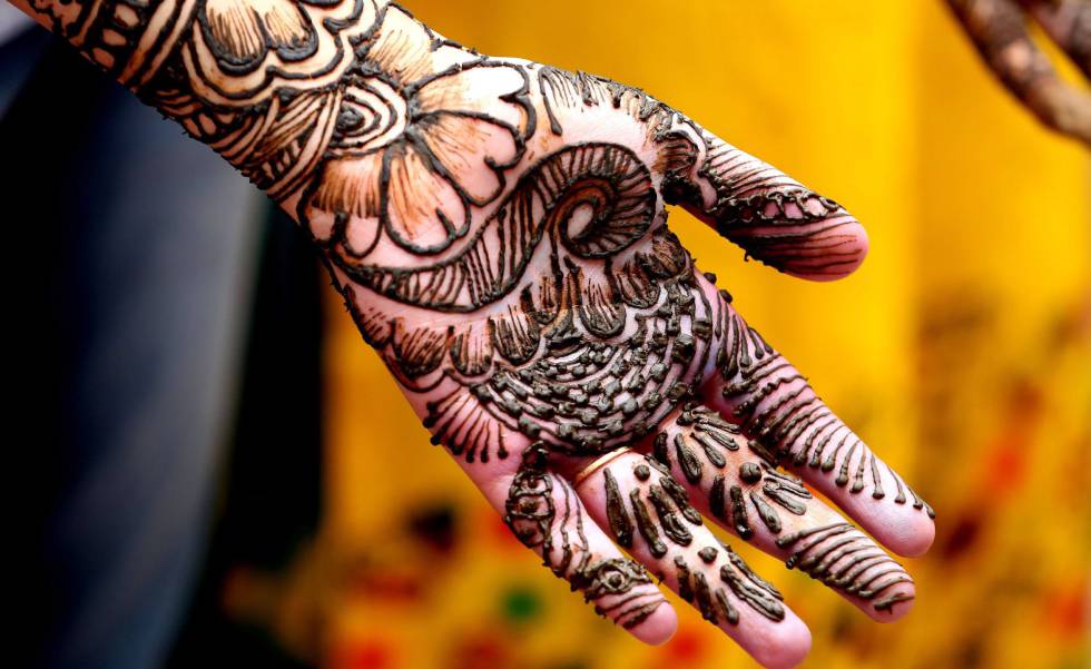 Estudante posa enquanto lhe fazem uma tatuagem de hena em Bhopal, na  Índia.