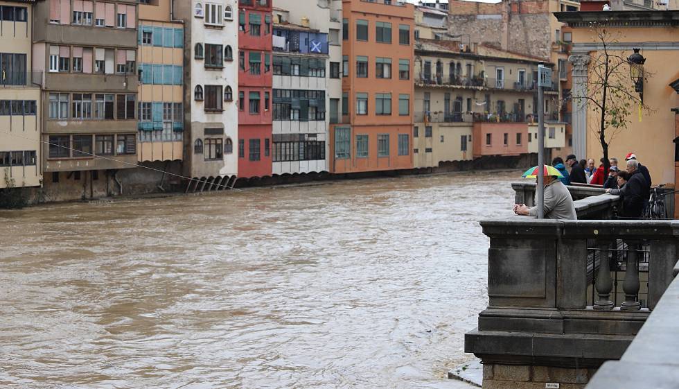 Varias personas contemplan el paso del río Onyar, desbordado por el temporal de lluvias.