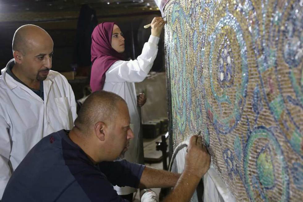 Restauradores palestinos retocan uno de los paneles superiores de mosaicos.