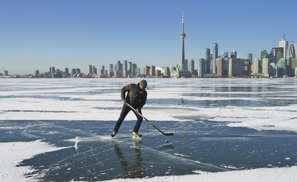 Un hombre juega al hockey con el 'skyline' de Toronto al fondo.